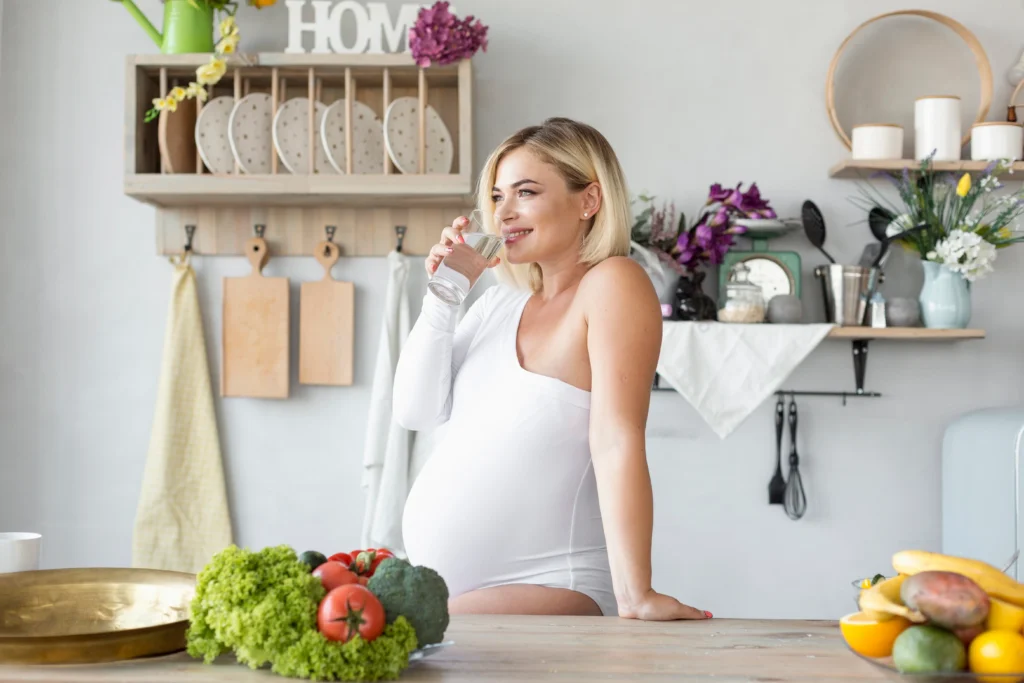 Mujer embarazada en una cocina con frutas y verduras para representar la alimentación durante el embarazo